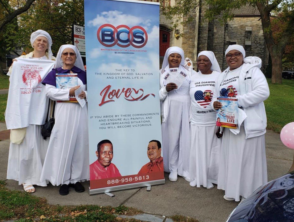 Women in white robes posing by banner