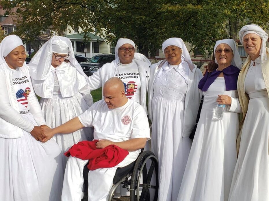 Women in white robes surrounding wheelchair user